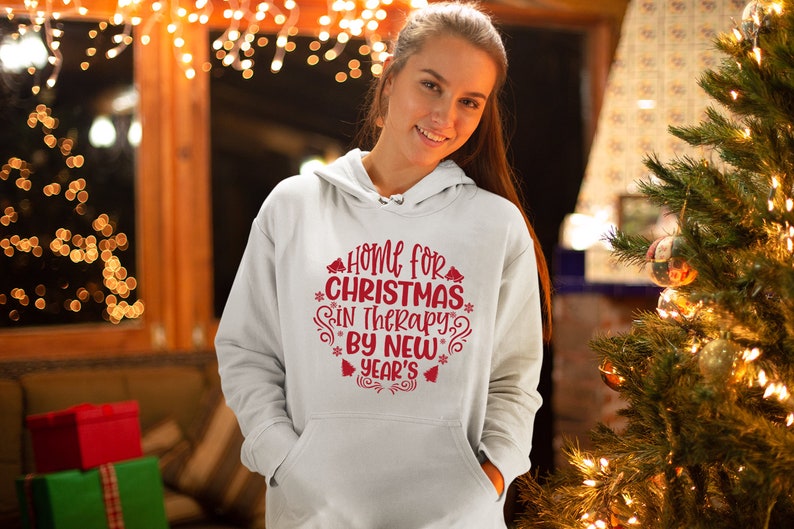 May include: White hoodie with red text that reads "Home for Christmas in Therapy by New Year's". The text is surrounded by snowflakes and bells.