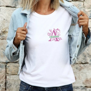 May include: A white t-shirt featuring a pink letter A with a green floral design. The letter A has the name "Anastasia" written across it.