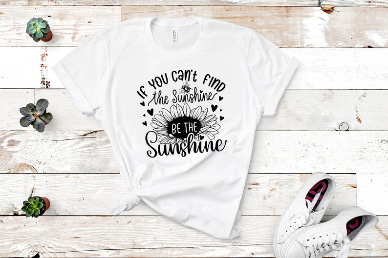May include: White t-shirt with a black sunflower graphic and the text "If you can't find the sunshine, be the sunshine".