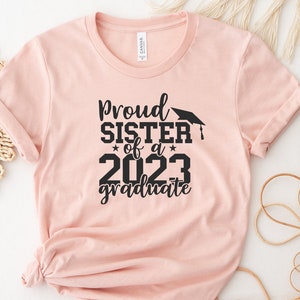 May include: A pink t-shirt with black text that reads "Proud Sister of a 2023 Graduate" with a graduation cap graphic.