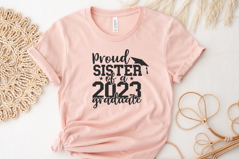 May include: A pink t-shirt with black text that reads "Proud Sister of a 2023 Graduate" with a graduation cap graphic.