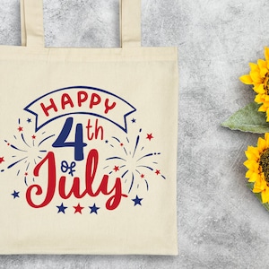 Peut inclure: Un sac fourre-tout en toile blanche avec un motif rouge, blanc et bleu qui dit "Happy 4th of July" avec des feux d'artifice et des &eacute;toiles.