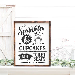 May include: A wooden sign with the text "Sprinkles are for cupcakes, not toilet seats". The sign features a black and white illustration of a cupcake with sprinkles.