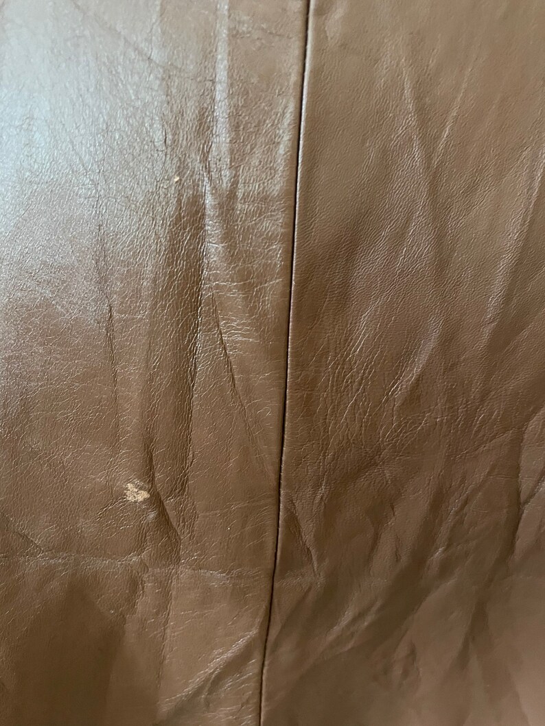 May include: Close-up of a brown leather surface with a subtle texture. The leather has a slight sheen and appears to be smooth and supple.