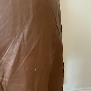 May include: A brown leather skirt with a slight sheen. The skirt is smooth and appears to be made of a high-quality material.