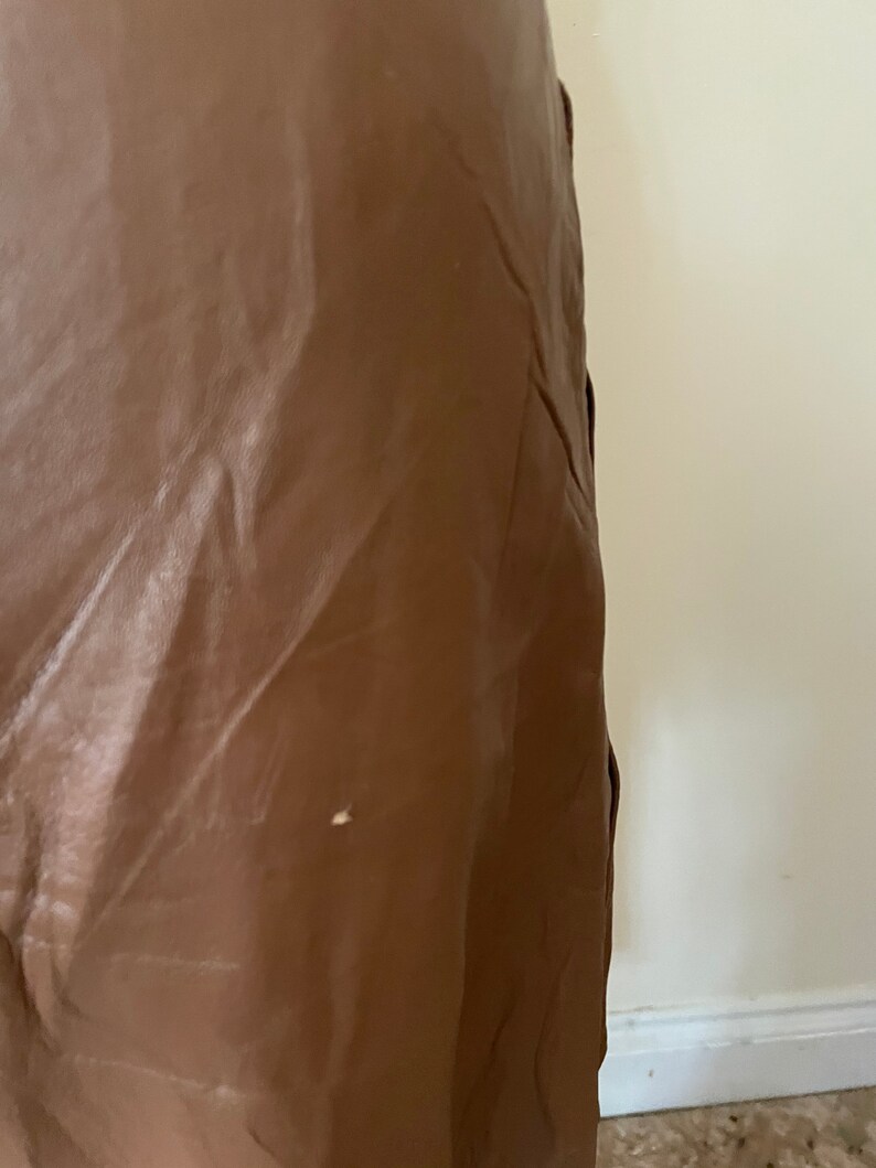 May include: A brown leather skirt with a slight sheen. The skirt is smooth and appears to be made of a high-quality material.