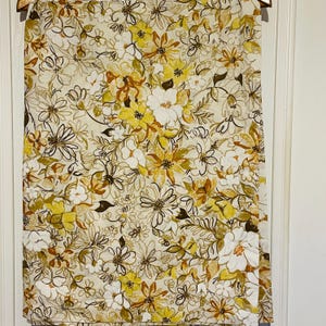 May include: A white fabric with a floral pattern in shades of yellow, brown, and white. The flowers are stylized and have a retro look.