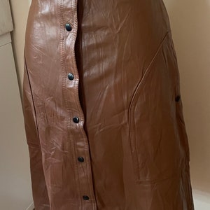 May include: A brown faux leather skirt with a button-up front and a side pocket. The skirt is knee-length and has a fitted waist.