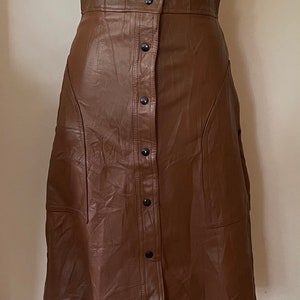 May include: A brown faux leather skirt with a button-up front and a slightly flared silhouette.