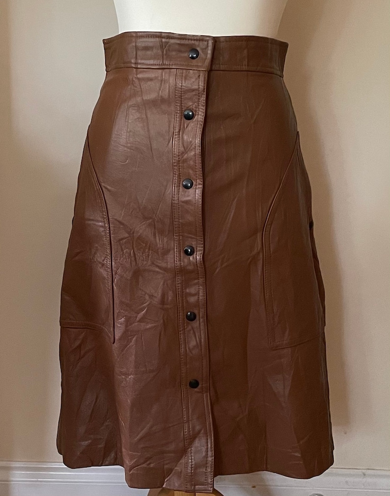 May include: A brown faux leather skirt with a button-up front and a slightly flared silhouette.