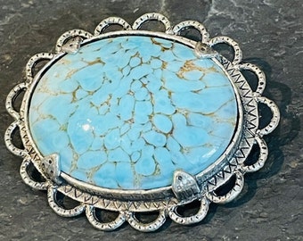 May include: A light blue oval-shaped brooch with a delicate silver filigree design. The brooch features a light blue stone with a marbled pattern.