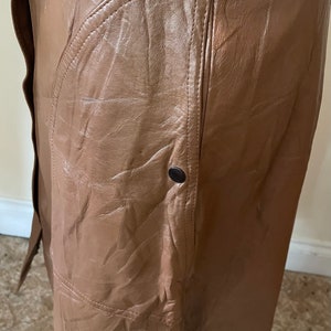 May include: A brown leather skirt with a large pocket on the side. The skirt has a button closure and a simple design.