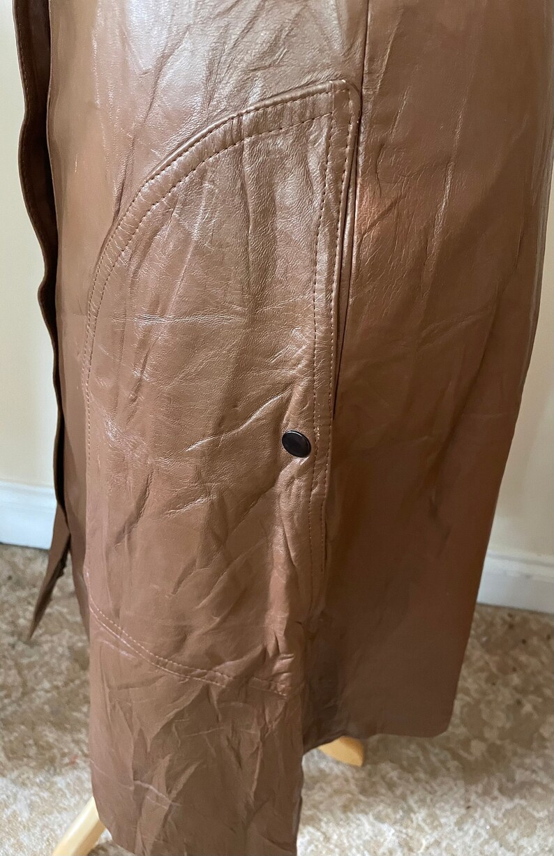 May include: A brown leather skirt with a large pocket on the side. The skirt has a button closure and a simple design.