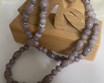 May include: A double-strand necklace made of lavender-colored oval beads with silver accents. The beads have a speckled pattern.