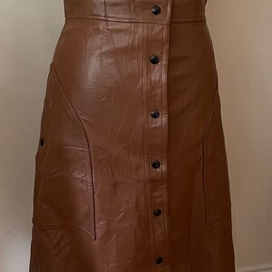 May include: A brown faux leather skirt with a button-up front and a slightly flared silhouette.