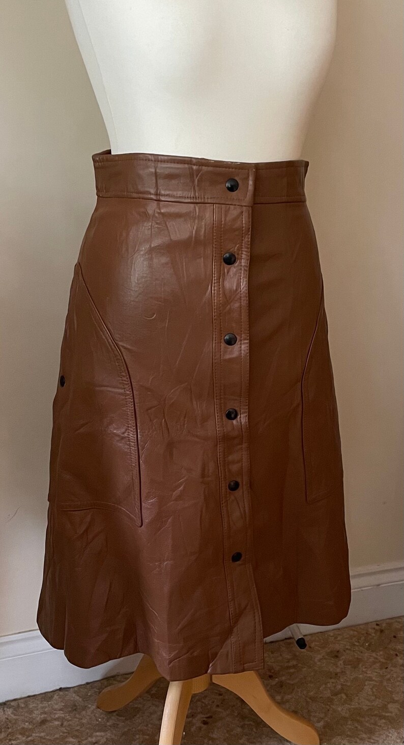 May include: A brown faux leather skirt with a button-up front and a slightly flared silhouette.