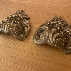 Puede incluir: Dos tiradores de cajón de metal adornados en tono dorado con intrincados diseños florales. Cada tirador tiene tres agujeros para su montaje.