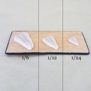 May include: Three pieces of raw fish on a wooden cutting board. The pieces are labeled 1/6, 1/12, and 1/24, indicating their relative sizes.