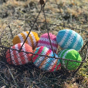 Peut inclure: Un panier en fil de fer avec une poignée en bois rempli d'œufs de Pâques tricotés colorés. Les œufs sont dans des tons de rose, bleu, vert, jaune et blanc.