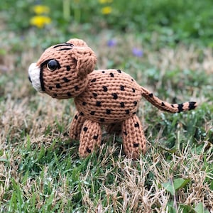 Puede incluir: Un juguete de guepardo de punto marrón y negro con ojos negros. El juguete está de pie sobre hierba verde.