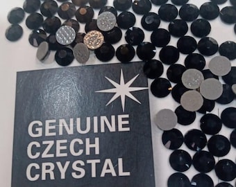 May include: Black, round crystal rhinestones scattered around a dark gray card. The card reads "GENUINE CZECH CRYSTAL" with a starburst design. Several silver-colored rhinestones are also present.