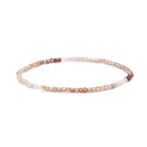 May include: A delicate beaded bracelet featuring small, round, translucent beads in shades of beige, tan, and soft brown. The strand is accented with a single, polished gold-toned spherical bead positioned near the center of the circular arrangement.