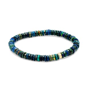 Könnte beinhalten: Ein Armband aus kleinen, facettierten, blauen und grünen Steinen. Eine einzelne goldfarbene Perle ist in das Armband eingesetzt. Das Armband ist für das Handgelenk konzipiert. Das Armband befindet sich auf weißem Hintergrund.