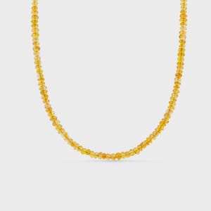 May include: A single strand necklace composed of numerous small, faceted, translucent golden-yellow beads. The beads are uniform in size and shape, strung together to form a continuous circular loop against a plain background.