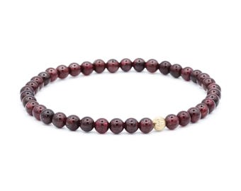 May include: A beaded bracelet featuring a continuous strand of small, round, deep red garnet beads. The bracelet is accented with a single, small, spherical gold bead that has a vertically ribbed texture, positioned slightly off-center.