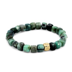 May include: A beaded bracelet featuring a series of faceted, cube-shaped green emerald beads arranged in a circular pattern, accented by a single, smooth, polished gold-toned cube bead positioned prominently among the natural green stones.