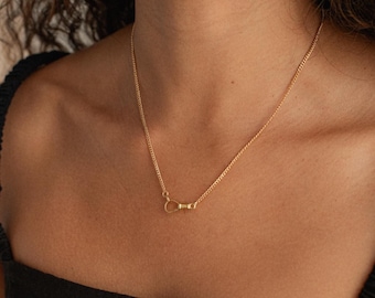 May include: A delicate gold necklace with a small, circular pendant. The necklace is a simple chain design, and the pendant is a small, minimalist detail. The necklace is worn against a dark background.