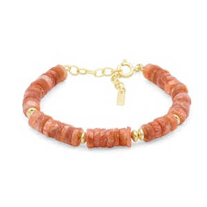 Puede incluir: Una pulsera con cuentas de piedra redondas y planas en tonos naranja, intercaladas con pequeñas cuentas de metal dorado pulido. La pieza incluye una cadena extensora dorada, un cierre de resorte circular y una pequeña etiqueta metálica rectangular.