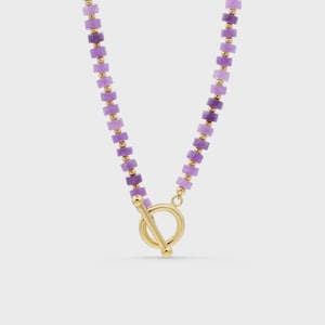 May include: A necklace featuring a series of small, cylindrical purple beads alternating with tiny gold-toned spherical spacers. The piece is secured with a gold-toned toggle clasp consisting of a circular ring and a T-shaped bar closure.