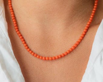 May include: A single strand necklace composed of small, uniform, round beads in a vibrant orange hue. The beads are strung together to form a continuous circular shape that rests against the neck, creating a simple and classic jewellery piece.