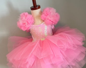 May include: A pink tulle dress with a sequined bodice and large pink tulle flower accents on the shoulders.