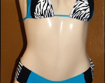 Puede incluir: Un traje de baño de dos piezas en un maniquí. La parte superior del bikini es de estilo halter con paneles azules, negros y estampados de cebra. La parte inferior a juego es azul con detalles negros y estampados de cebra. El traje de baño se exhibe en un maniquí.
