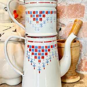 Könnte beinhalten: Eine weiße Emaille-Kaffeekanne mit einem roten und blauen geometrischen Muster. Die Kanne hat einen Deckel und einen Ausguss. Die Kanne steht auf einer Arbeitsplatte.