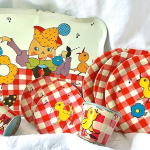 Könnte beinhalten: Ein Vintage-Kinderspielzeug-Tee-Set mit einem rot-weiß karierten Muster. Das Set enthält ein Tablett, vier Teller, zwei Tassen und eine Teekanne. Das Tablett zeigt eine skurrile Illustration einer Figur mit einer Blume und einem Vogel.