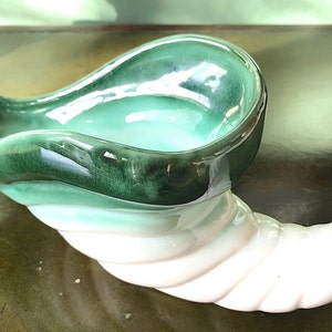 May include: A green and white ceramic cornucopia with a swirling design. The cornucopia is a traditional symbol of abundance and prosperity.