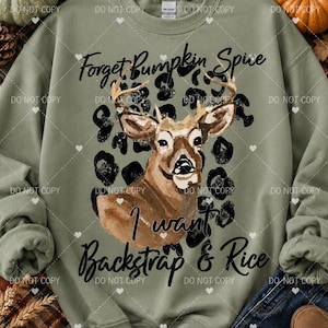 May include: An olive green crewneck sweatshirt featuring a central graphic of a brown deer head layered over a black leopard print pattern. The text "Forget Pumpkin Spice I want Backstrap & Rice" is printed in black script above and below the deer.
