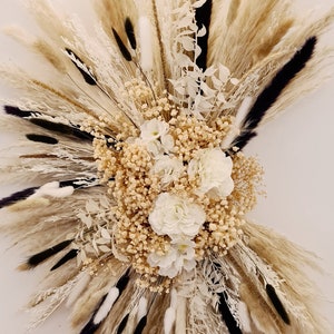 May include: A dried floral arrangement with white flowers and pampas grass in shades of beige and black.