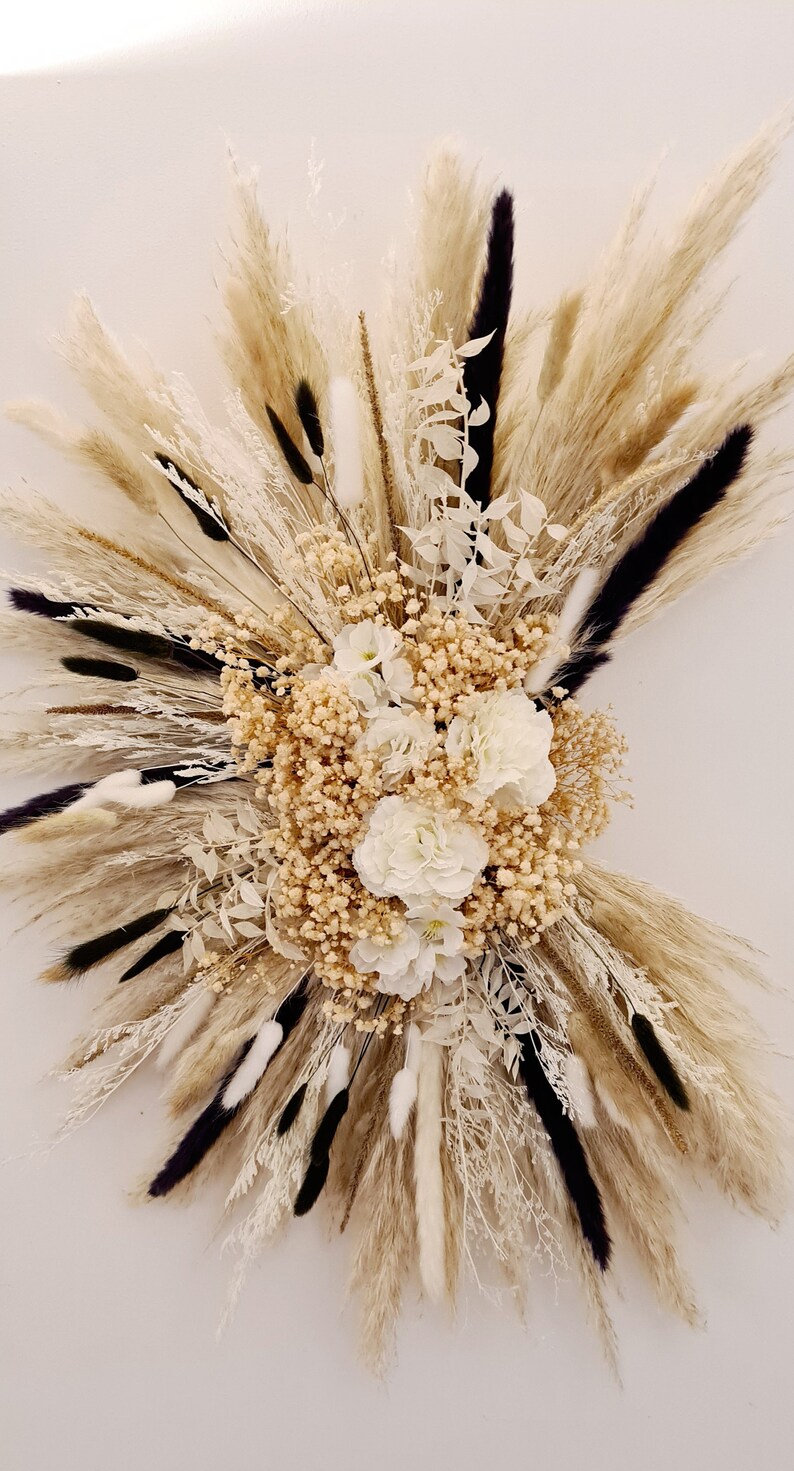 May include: A dried floral arrangement with white flowers and pampas grass in shades of beige and black.