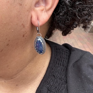 May include: Silver earrings with a blue gemstone set in a silver oval frame.