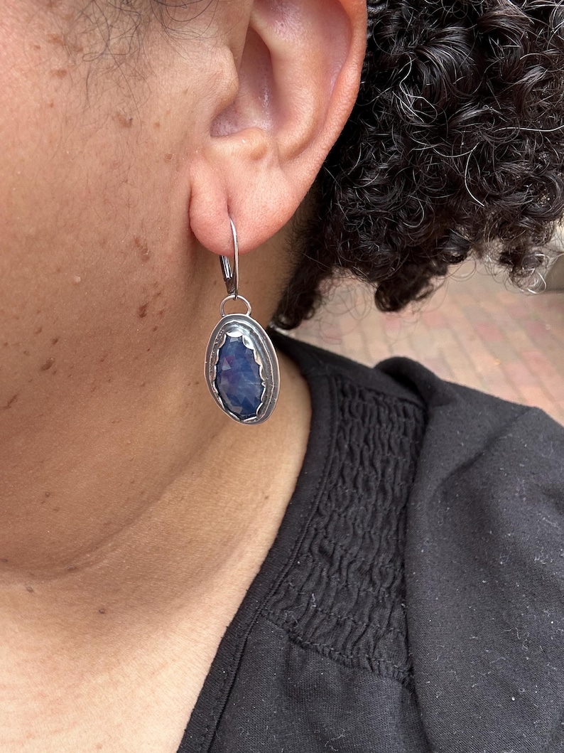 May include: Silver earrings with a blue gemstone set in a silver oval frame.