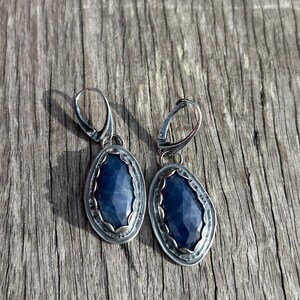 May include: A pair of silver earrings with blue gemstone accents. The earrings have a simple, elegant design and are perfect for everyday wear.