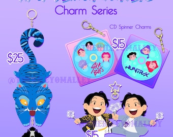 May include: A promotional image for KPOP DEMON HUNTERS Charm Series. It features a blue tiger charm, CD spinner charms, and Bobby charms with glimmer. The text includes "Derpy & Sussy Dangle Charm" and "Bobby Charm w/ glimmer".