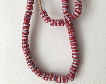 May include: A long necklace made of red and white striped glass beads with blue accents. The beads are strung on a natural fiber cord.