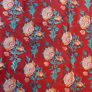May include: Red fabric with a repeating floral pattern. The flowers are pink, orange, and yellow with green leaves. The background is a deep red.