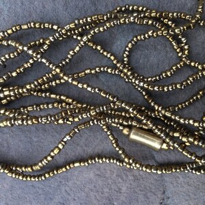 K&ouml;nnte beinhalten: Eine goldene Perlenkette mit einem goldenen Metallverschluss. Die Kette besteht aus kleinen, runden Perlen, die zu einer langen Schnur zusammengef&uuml;gt sind.