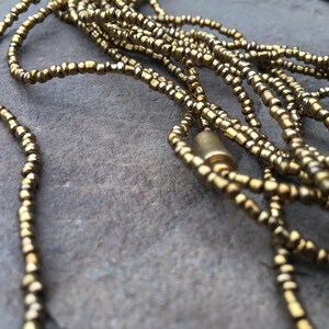 K&ouml;nnte beinhalten: Eine goldene Perlenkette mit einem goldenen Metallverschluss. Die Kette besteht aus mehreren Perlenstr&auml;ngen und liegt auf einer grauen Oberfl&auml;che.